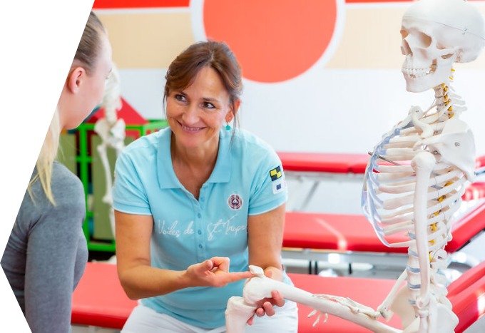 Eine Person in einem hellblauen Hemd zeigt auf das Kniegelenk eines menschlichen Skelettmodells, während eine andere Person zuschaut.